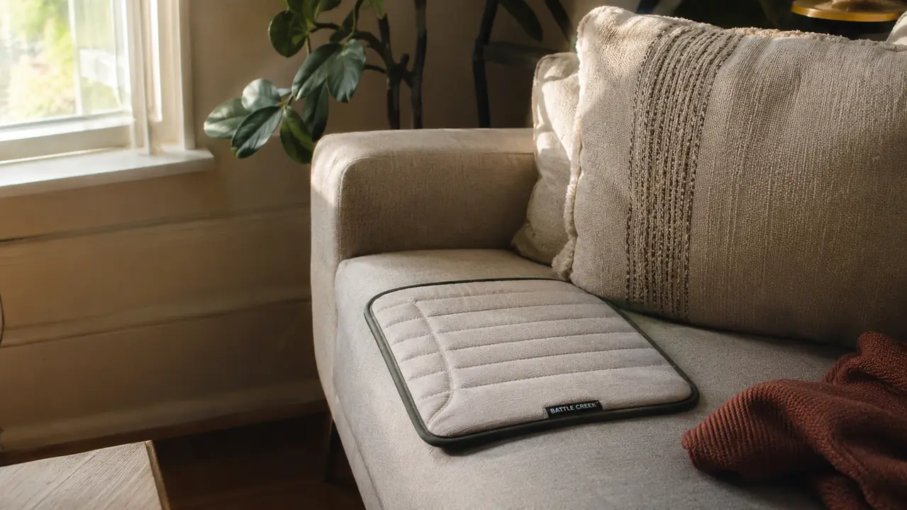 a flat self-warming pad on the end of a couch near a window in morning light